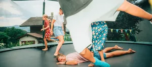 25-09-verantwortung-teilen-mental-load-dossier-schweizer-elternmagazin-hgload- Verantwortung teilen, Dossier Mental Load: Mutter liegt auf Trampolin am Boden, Kinder hüpfen