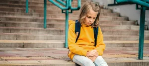 Schulwechsel. Junges Mädchen sitzt betrübt auf einer Treppe. Schulwechsel. Junges Mädchen sitzt betrübt auf einer Treppe.