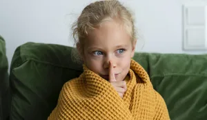 Contemplative girl wrapped in blanket making silence gesture at home Hochsensible Kinder reagieren oft empfindlicher auf Lärm