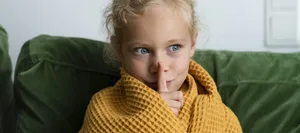 Contemplative girl wrapped in blanket making silence gesture at home Hochsensible Kinder reagieren oft empfindlicher auf Lärm