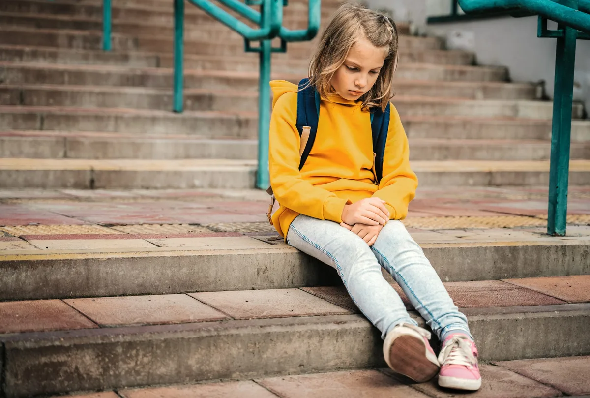 Changement d'école. Une jeune fille est assise sur un escalier, l'air triste. Changement d'école. Une jeune fille est assise sur un escalier, l'air triste.