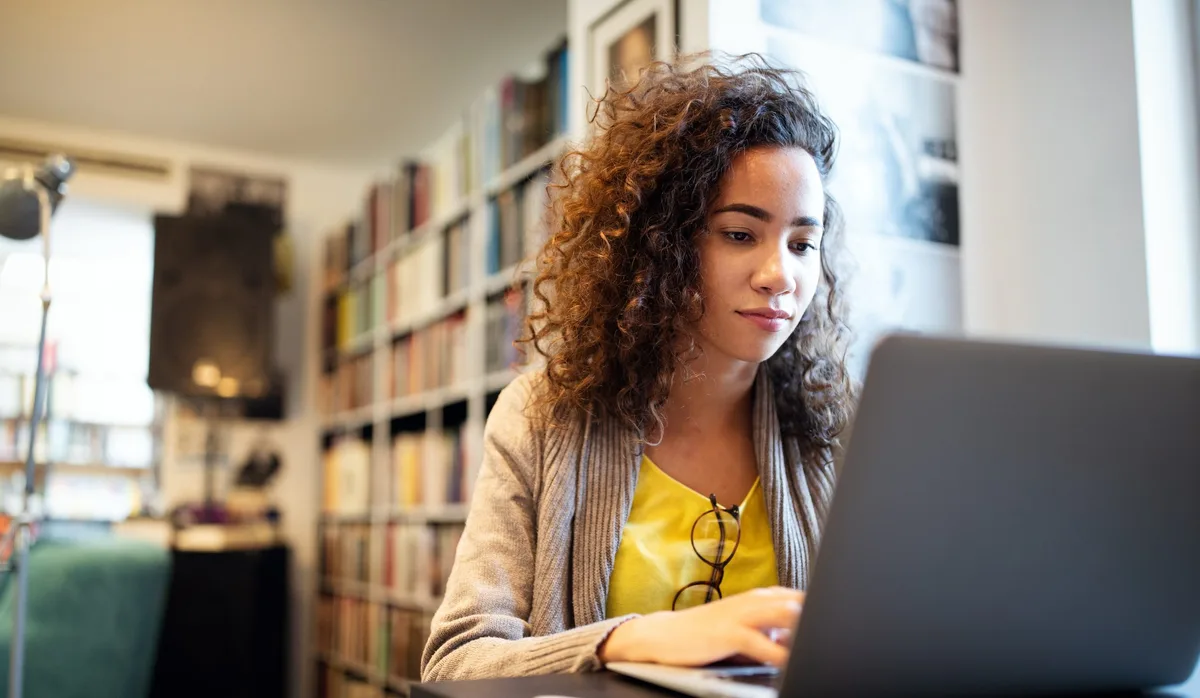 Une jeune et jolie étudiante qui travaille et étudie à la bibliothèque de l’université L'IA pour postuler à un emploi ? Une jeune fille est assise devant son ordinateur portable
