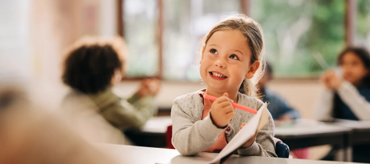 Young girl drawing in classroom during back to school season Motiviert lernen: Ein Mädchen sitzt begeistert im Schulzimmer
