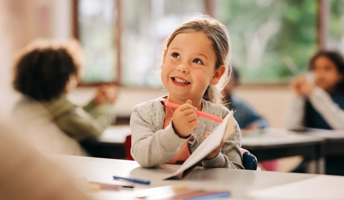 Young girl drawing in classroom during back to school season Motiviert lernen: Ein Mädchen sitzt begeistert im Schulzimmer