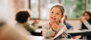 Young girl drawing in classroom during back to school season Motiviert lernen: Ein Mädchen sitzt begeistert im Schulzimmer