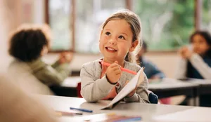 Young girl drawing in classroom during back to school season Motiviert lernen: Ein Mädchen sitzt begeistert im Schulzimmer