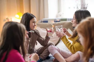 A group of young girls sitting on a bed, eating. Accommodation: Friends get together for a pyjama party