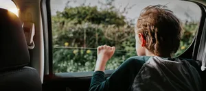 Young boy in the back of a car looks out of the window on a sunny day Trennung: Ein Junge schaut aus einem fahrenden Auto