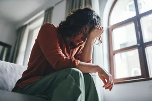 A distressed woman sitting on a sofa in a sunny flat A distraught woman is sitting on the bed