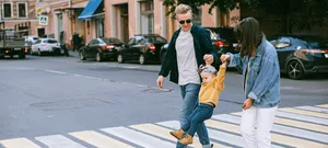 Header_new_family_feeling_Irena_Ristic Corona and family: Mother and father walk across a zebra crossing and rock the child in the middle.