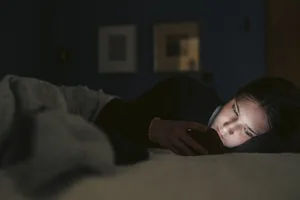 Una ragazza che naviga sullo smartphone mentre è sdraiata sul letto nella sua camera da letto di notte Ragazza che scorre lo schermo del proprio smartphone