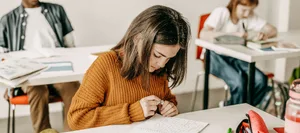 schule-lch-sandra-locher-benguerel-schweizer-elternmagazin-hg Volksschule. Ein Mädchen sitzt im Klassenzimmer und schreibt.