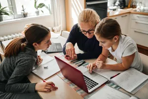 Homeschooling – Mother helping her daughters to finish school homework during coronavirus quarantine Learning with AI: A mother helps her two daughters with their homework