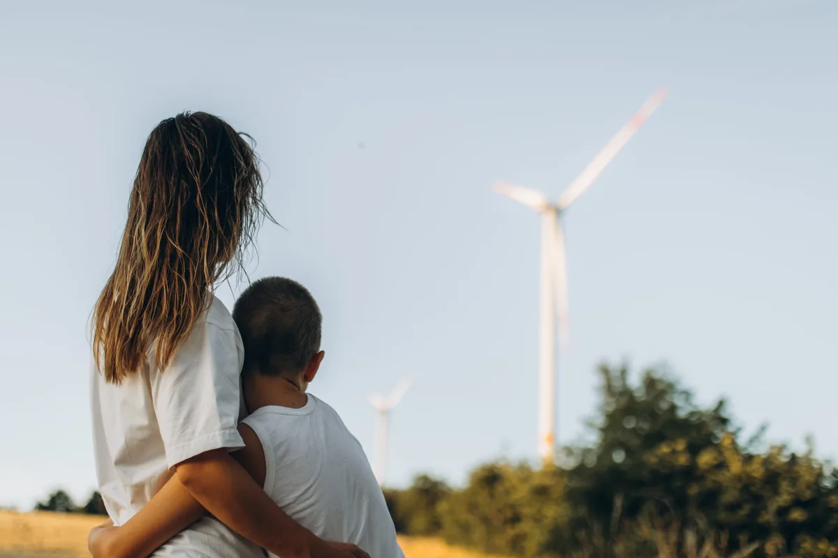 Une mère et son fils, vus de dos devant un moulin à vent. Changement climatique : une mère et son fils se tiennent devant une éolienne