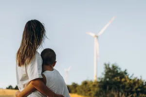 Une mère et son fils, vus de dos devant un moulin à vent. Changement climatique : une mère et son fils se tiennent devant une éolienne